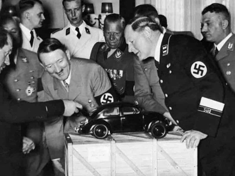 Ferdinand Porsche (links met uitgestrekte arm) toont Adolf Hitler zijn prototype van de latere Volkswagen Kever