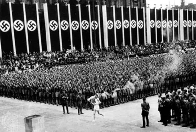 De laatste fakkeldrager komt binnen in het Olympisch Stadion, versierd met hakenkruizen